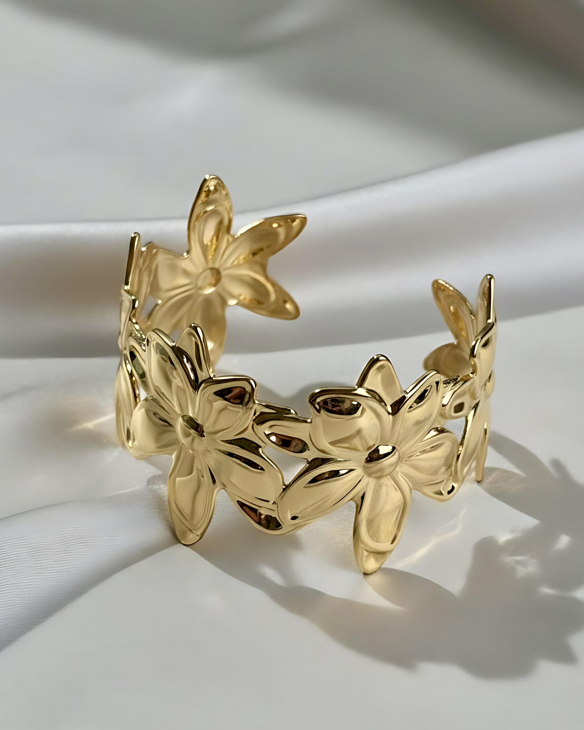 Wide Gold Flower Cuff Bracelet - Statement Botanical Jewellery A wide gold open cuff bracelet featuring a large, continuous floral cutout motif with overlapping flower shapes, resting on a white silk background.