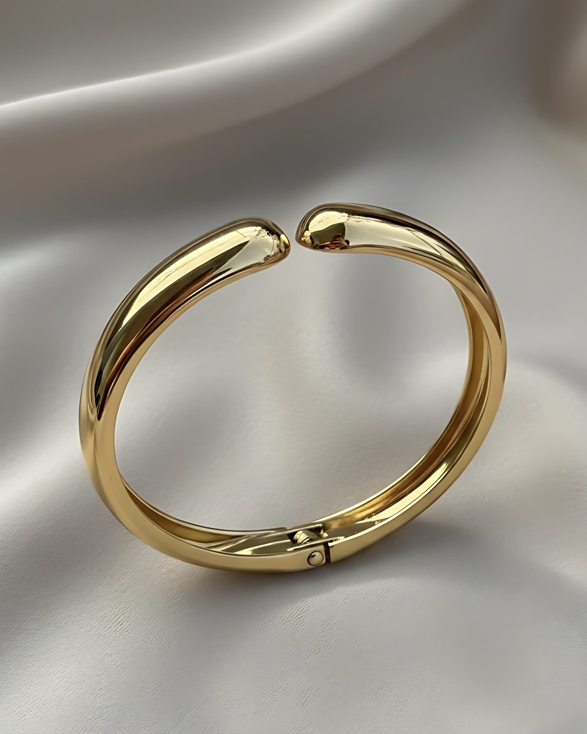 Chunky Gold Torque Bangle - Sculptural Open Cuff Jewellery A wide, high-polished gold hinged bangle bracelet featuring a sleek, sculptural torque or open cuff design with rounded ends, resting on a white silk background.