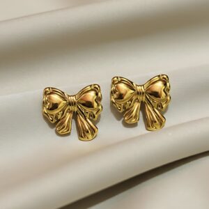 A pair of gold stud earrings featuring a three-dimensional, puffy ribbon bowknot design with a high-polish finish, resting on white silk.