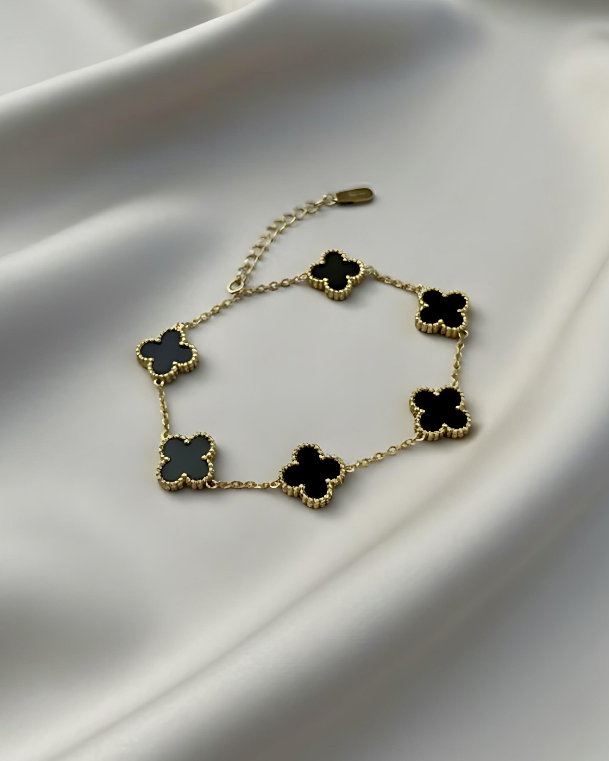 Dual-Sided Black and White Clover Bracelet-Adjustable Gold Link Jewellery A gold link bracelet featuring five four-leaf clover charms. The charm visible is black enamel with a beaded gold border. This design is reversible to white mother-of-pearl.