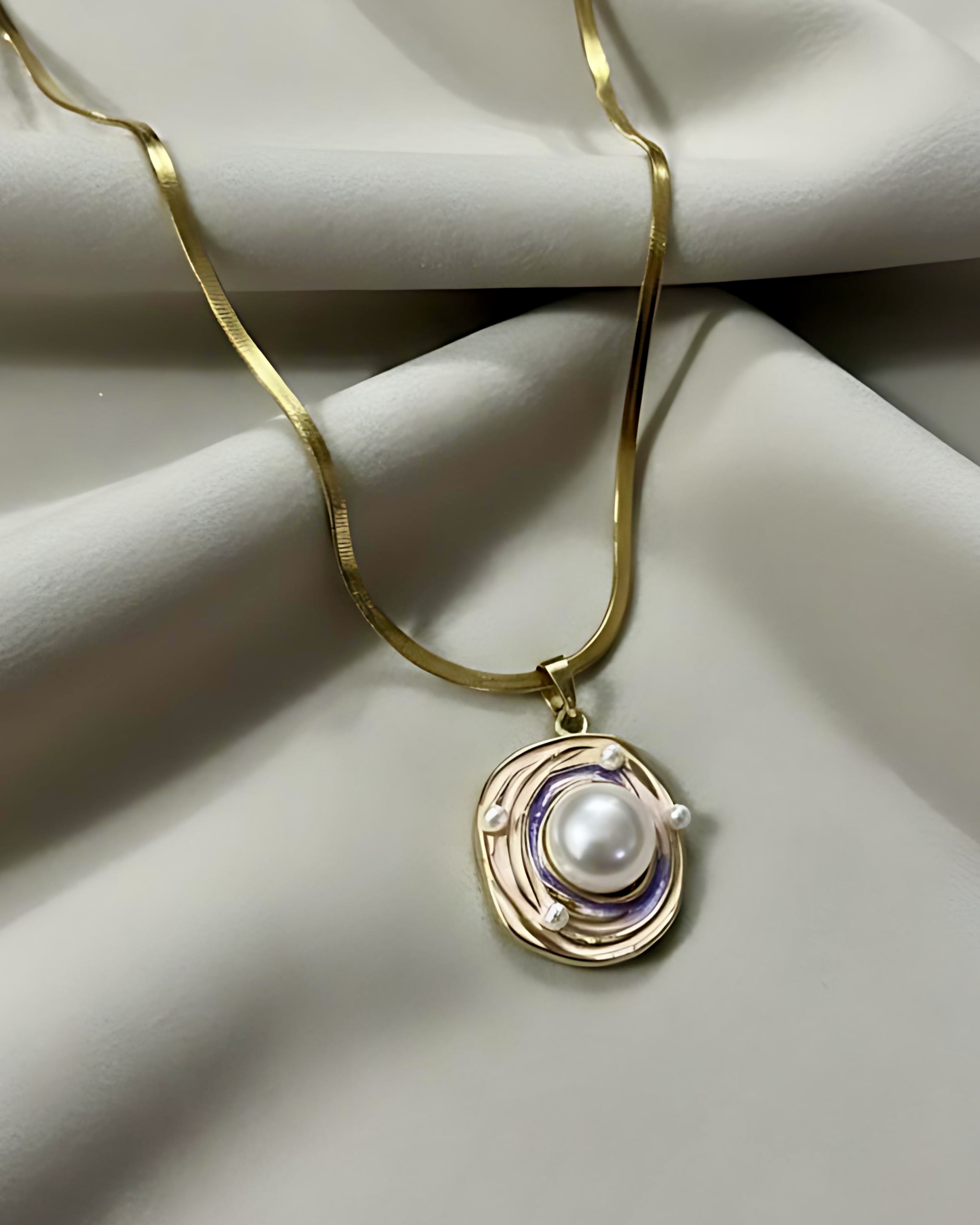 Gold Swirl Enamel Pearl Pendant Necklace on Snake Chain A gold snake chain necklace with an oval pendant featuring a central white pearl surrounded by abstract pink and lilac enamel swirls and small seed pearls, resting on white silk.